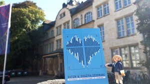 Spielfigur von Friedrich Schiller h?lt Postkarte mit Balkendiagrammen, die wie ein Herz aussehen